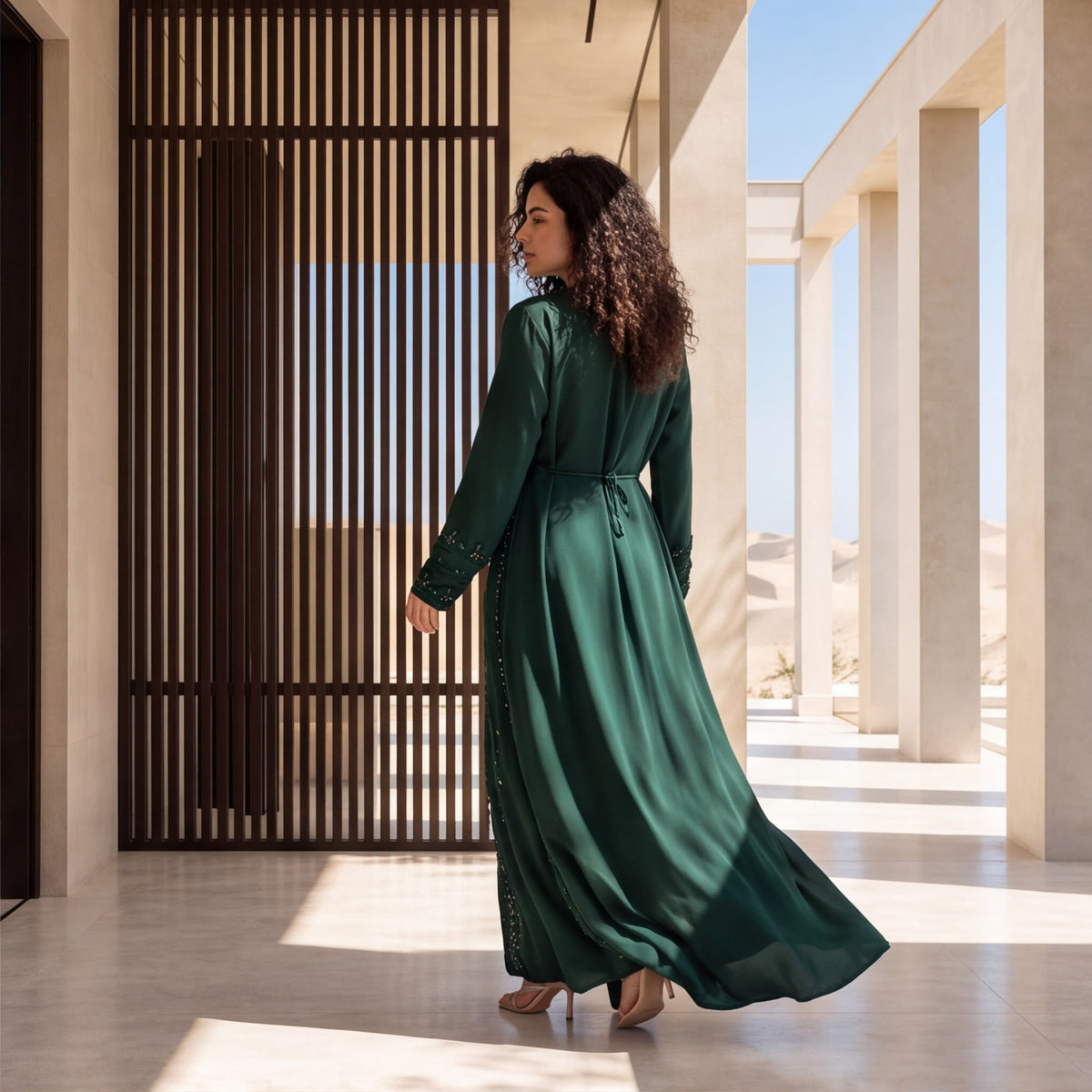 Back view of a woman wearing a floor-length emerald green kaftan with beaded embroidery detailing.