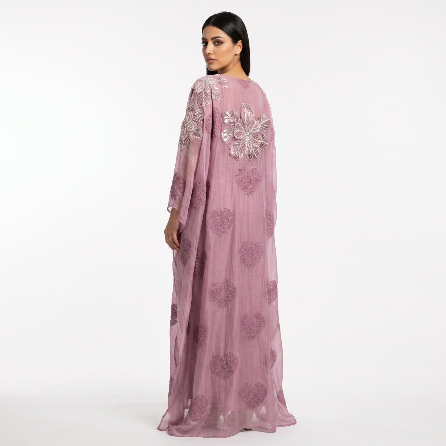A woman modeling a long, sheer mauve-pink kaftan dress with floral embroidery and sequin embellishments, shown from the back against a plain white studio background.