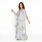 A woman modeling a long, flowing white caftan dress with silver sequin and bead embroidery, set against a plain white studio background.