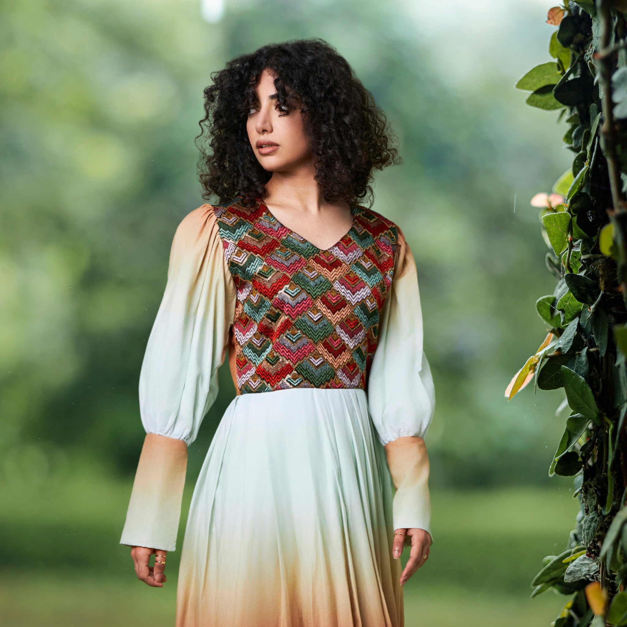 Woman wearing a patterned top and gradient organic dress standing outdoors with greenery in the background