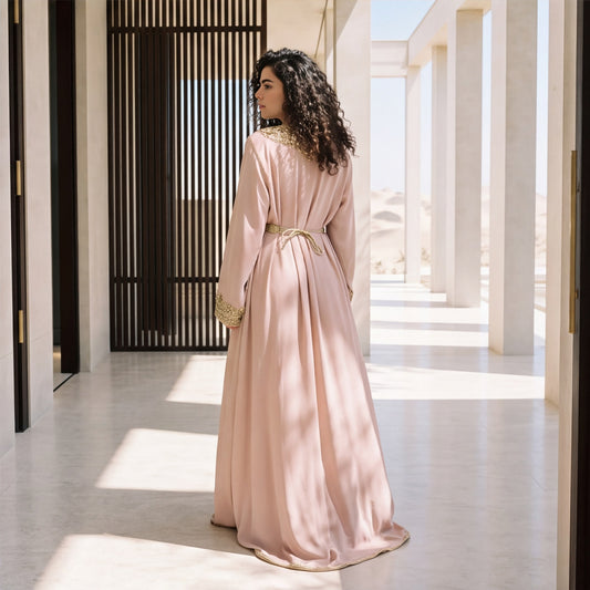 Back view of a woman wearing a floor-length blush pink handmade Moroccan kaftan with gold scroll trim.