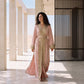 A woman wearing a rich dusty rose floor-length kaftan with ornate gold beaded lace embroidery, standing in a sunlit setting.