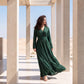 A woman wearing an emerald green kaftan with beaded stripe embroidery and a gold belt, in a Moroccan architectural setting.