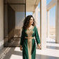 Back view of a woman wearing an emerald green floor-length kaftan with gold filigree embroidery.