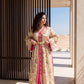 A woman wearing a long beige and pink floral robe with gold trim and a matching belt, standing in a modern outdoor setting with a slatted wooden screen and desert landscape in the background.
