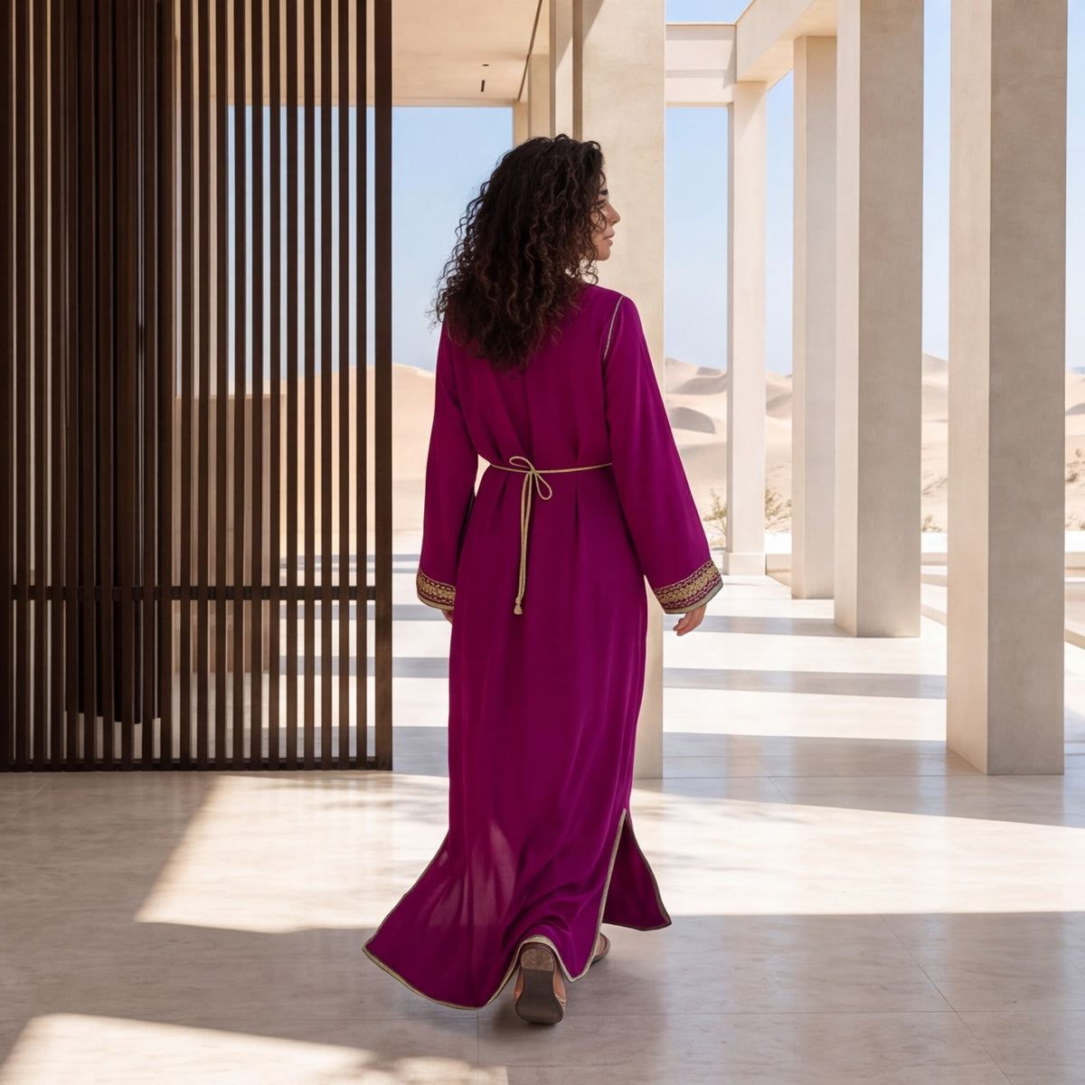 Back view of a woman wearing a floor-length magenta kaftan with a gold belt.