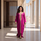 A woman wearing a vibrant magenta floor-length kaftan, standing in a sunlit architectural setting.
