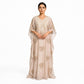A woman modeling a floor-length beige caftan dress with gold embroidery and sheer draped sleeves against a plain white background.