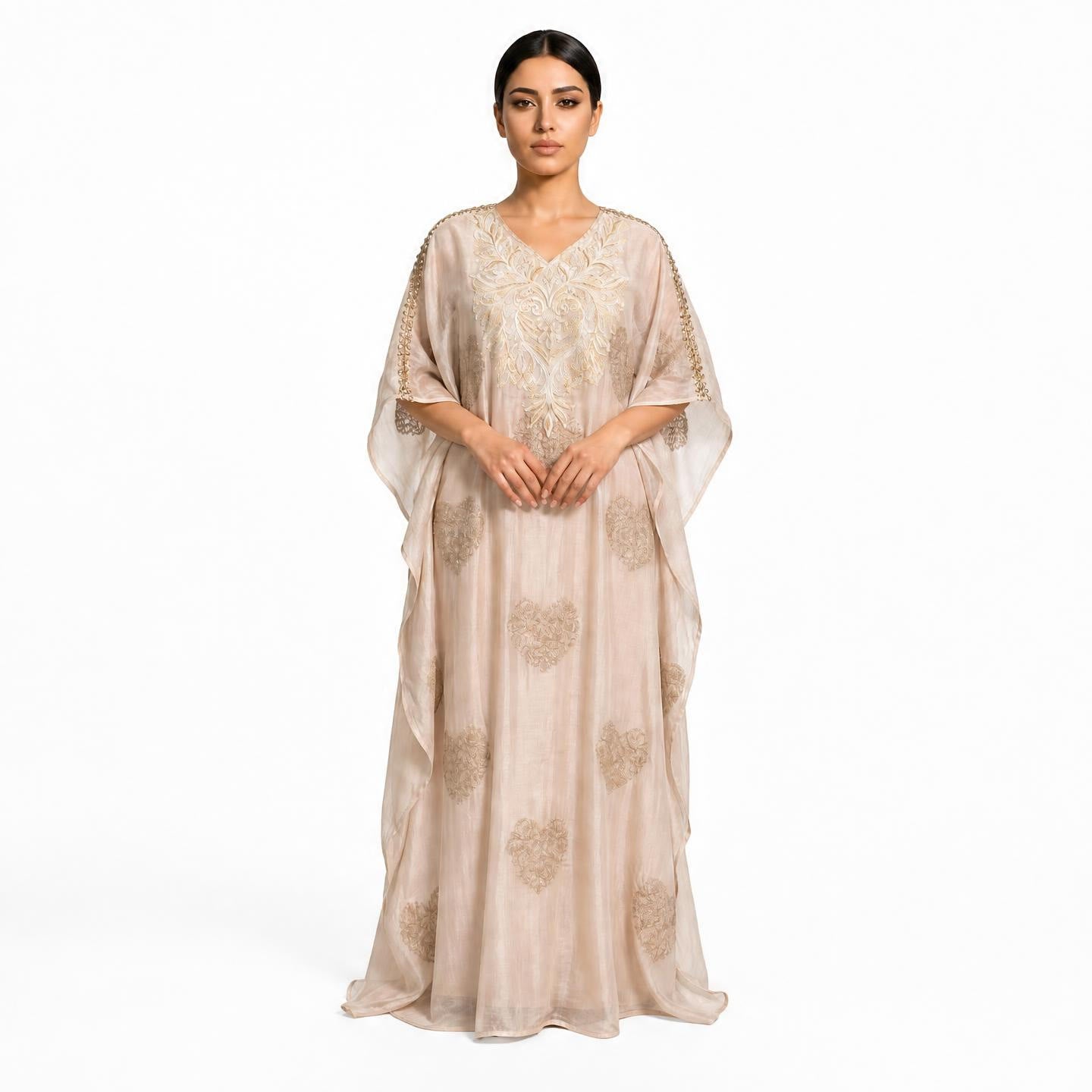 A woman modeling a floor-length beige caftan dress with gold embroidery and sheer draped sleeves against a plain white background.