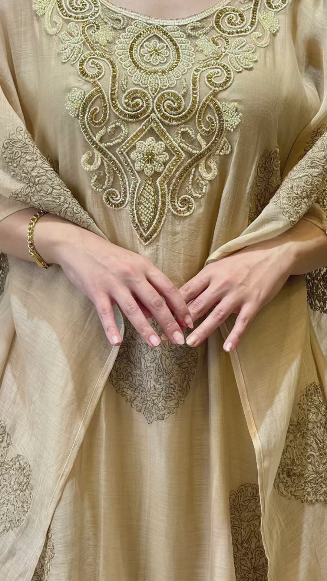 A short aesthetic video loop of the luxury beige 2-piece mul cotton kaftan, showcasing the heavy gold embroidery on the neck and sleeves and the elegant drape of the Armani silk inner in motion.