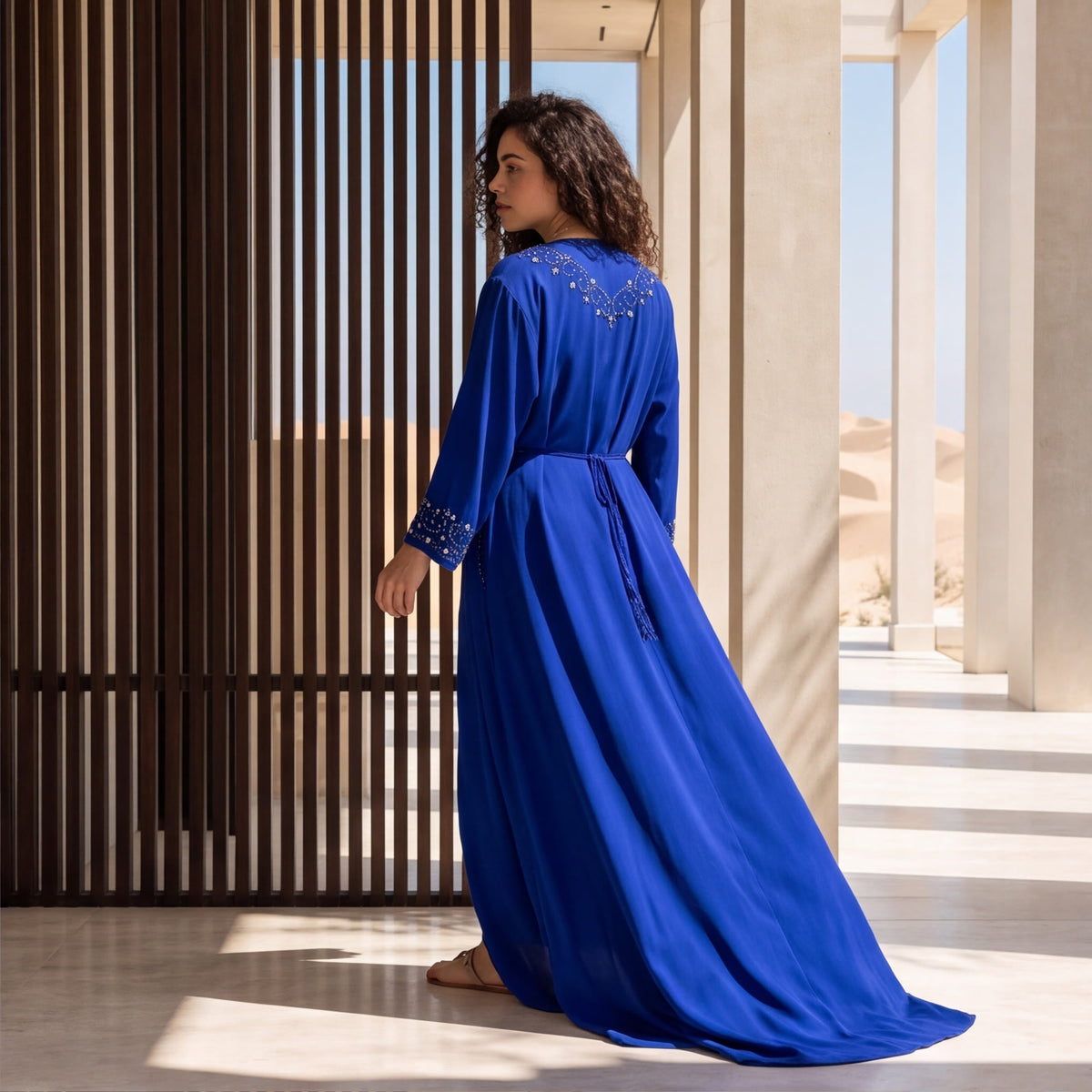 Back view of a woman wearing a floor-length royal blue kaftan with beaded embroidery detailing.