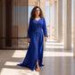 A woman wearing a striking royal blue floor-length kaftan with silver and crystal beaded embroidery, standing in a sunlit setting.