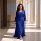 A woman wearing a royal blue kaftan with silver and crystal beaded embroidery and a matching belt, in a Moroccan architectural setting.