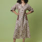 A woman modeling a long-sleeved midi dress with a brown and beige floral print, standing against a solid sage green studio background.