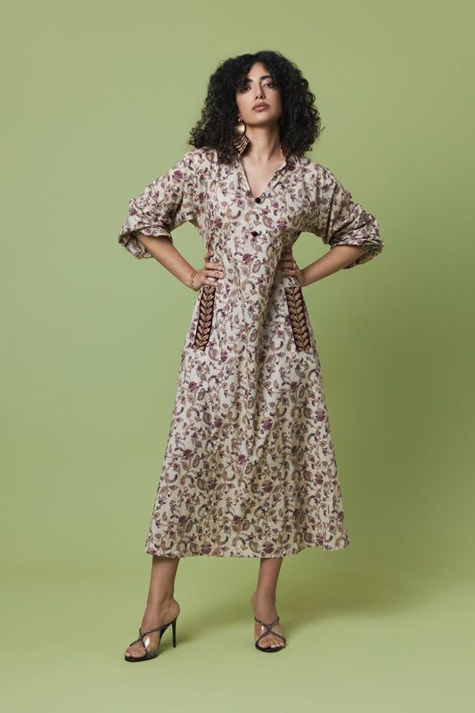 A woman modeling a long-sleeved midi dress with a brown and beige floral print, standing against a solid sage green studio background.