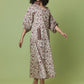 A woman modeling a long-sleeved midi dress with a beige and brown floral pattern, lace-up front detail, and black strappy heels, set against a solid light green studio background.