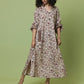 A woman modeling a long-sleeved midi dress with a beige and brown floral pattern, standing against a solid sage green studio background.