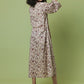 A woman with curly black hair is shown from the back wearing a long-sleeved midi dress with a dense floral print in brown and muted red on a cream background. She is posing against a solid light green studio backdrop.