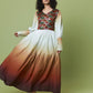 A woman modeling a long-sleeved maxi dress with a multicolor geometric patterned bodice and a flowing white-to-brown ombre skirt, set against a solid sage green studio background.