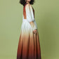 A woman modeling a long-sleeved maxi dress with a vertical gradient design, transitioning from white at the top to rust orange and deep brown at the bottom, set against a solid sage green studio background.