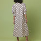 A woman viewed from behind wearing a long-sleeved midi dress with a black trellis pattern on a cream background, paired with black high heels, set against a solid light green studio backdrop.