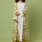 A woman modeling a long olive green and cream printed kaftan robe over a cream dress, standing against a solid olive green studio background.