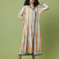 A woman modeling a long-sleeved, midi-length kaftan dress with vertical stripes in yellow, orange, pink, and white, accented with teal trim, set against a solid light green studio background.