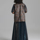 A model viewed from the back wearing a long dark teal-blue sheer skirt with a patterned brown vest layered over sheer sleeves, set against a solid gray studio background.