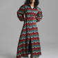 A model wearing a long-sleeved, collared maxi dress with a vibrant multicolor chevron pattern in red, teal, cream, and brown, standing against a neutral gray studio background.