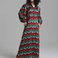 A woman modeling a long-sleeved maxi dress with a vibrant multicolor chevron pattern in red, teal, green, and cream, set against a plain gray studio background.