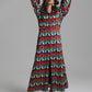 A woman modeling a long-sleeved maxi dress with a vibrant multicolor chevron pattern in red, teal, yellow, and white, set against a plain gray studio background.