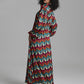 A model wearing a long-sleeved maxi dress with a vibrant multicolor chevron pattern, photographed against a neutral gray studio background.