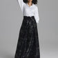 A model wearing a white long-sleeve button-up shirt and a high-waisted black maxi skirt with a silver floral jacquard pattern, posed against a solid gray studio background.