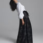 A model wearing a long black skirt with a silver floral jacquard pattern and a white blouse, posing in profile against a solid gray studio background.