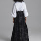 A model shown from the back wearing a white blouse with voluminous three-quarter sleeves and a long black skirt featuring a subtle tonal floral pattern, set against a solid gray studio background.