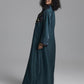 A woman modeling a long, dark teal abaya with intricate multicolor embroidery around the neckline and cuffs, photographed against a neutral gray studio background.