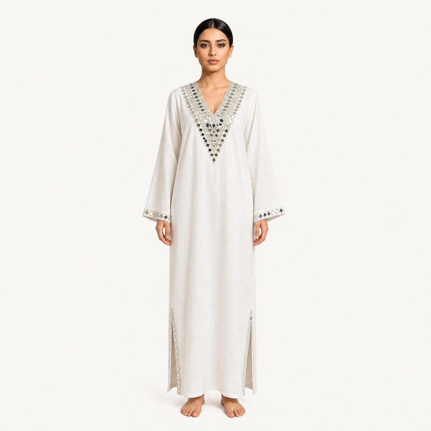 Woman wearing an ivory pure linen kaftan with silver mirror-embroidered V-neckline, front view
Description: Front view of the RUBEENA AMEEN pure linen kaftan in ivory white, featuring silver mirror-work embroidery at the neckline and side slits, with a relaxed floor-length silhouette.