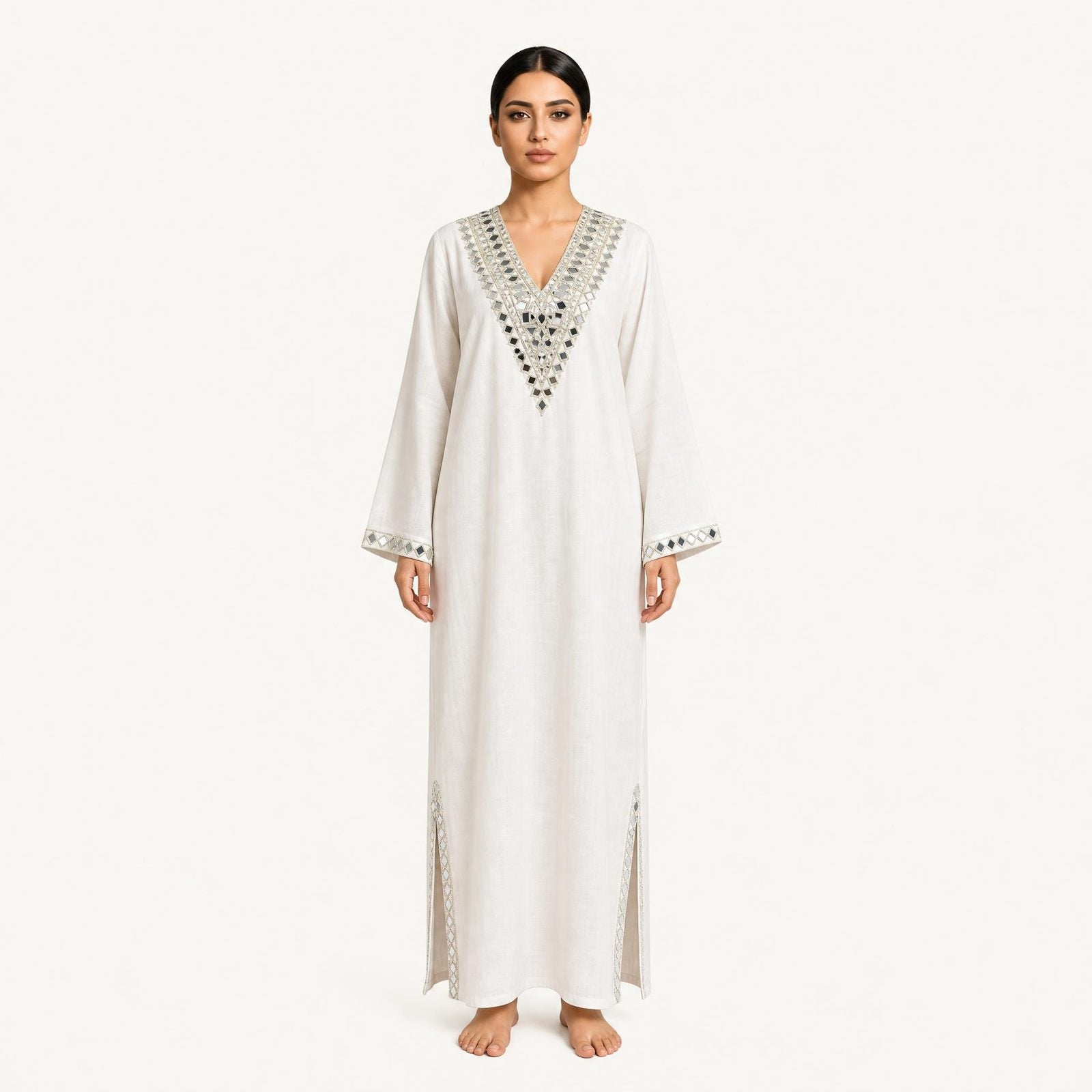Woman wearing an ivory pure linen kaftan with silver mirror-embroidered V-neckline, front view
Description: Front view of the RUBEENA AMEEN pure linen kaftan in ivory white, featuring silver mirror-work embroidery at the neckline and side slits, with a relaxed floor-length silhouette.