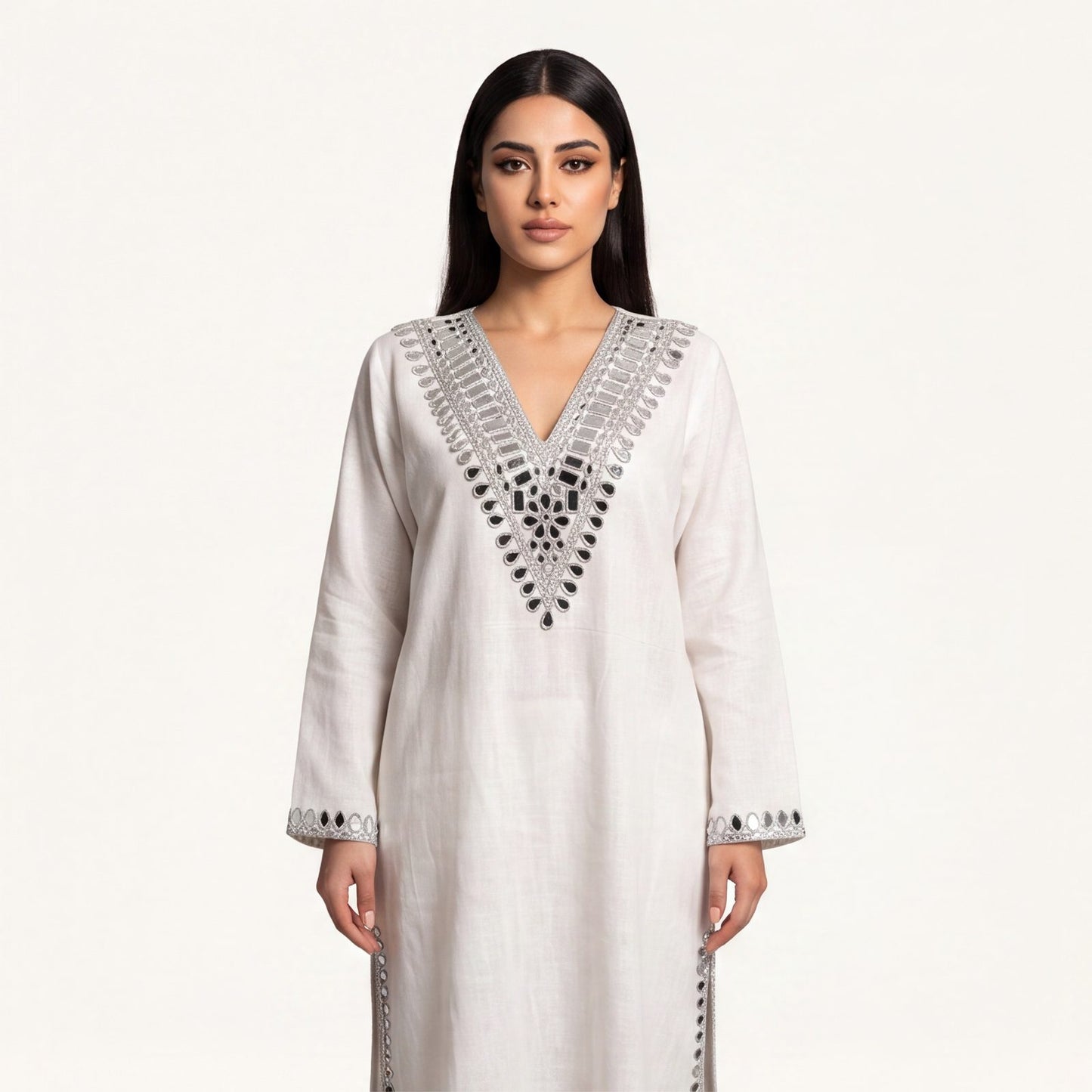 A woman modeling a long-sleeved white kurta with silver mirror work embroidery around the V-neck and cuffs, set against a plain off-white background.