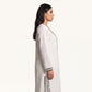 Side profile of ivory pure linen kaftan showing flowing silhouette and mirror-trimmed side slit
Description: Side profile view of the pure linen kaftan in ivory white, showing the floor-length drape and silver mirror-trimmed side slit detail.