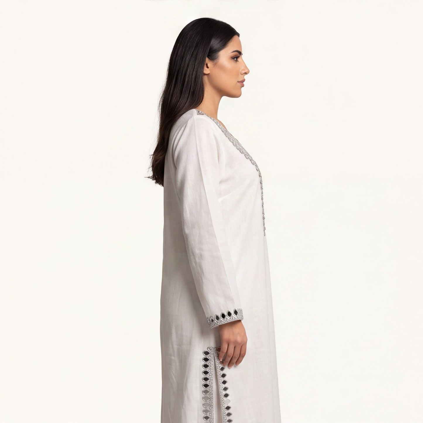 Side profile of ivory pure linen kaftan showing flowing silhouette and mirror-trimmed side slit
Description: Side profile view of the pure linen kaftan in ivory white, showing the floor-length drape and silver mirror-trimmed side slit detail.