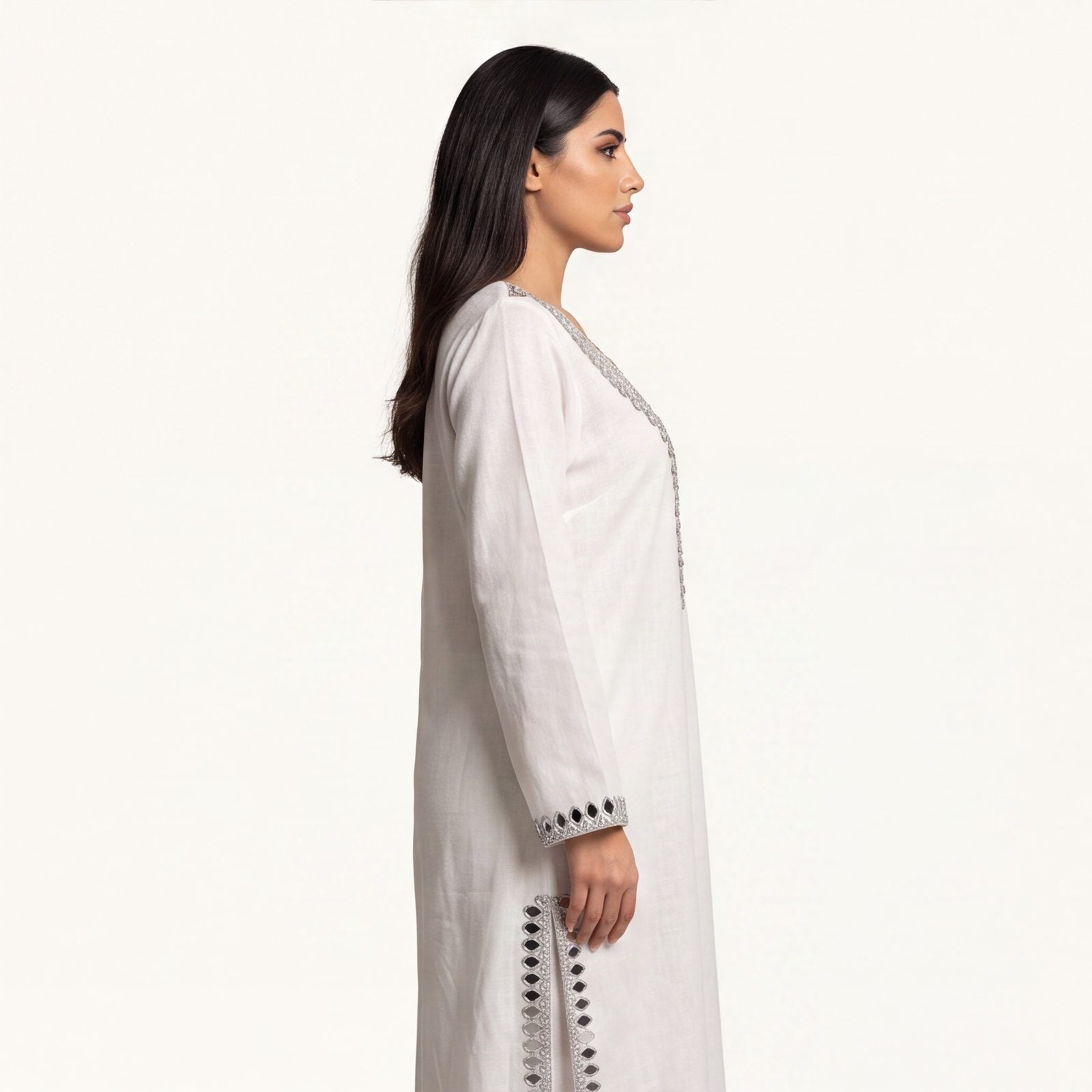 Side profile of ivory pure linen kaftan showing flowing silhouette and mirror-trimmed side slit
Description: Side profile view of the pure linen kaftan in ivory white, showing the floor-length drape and silver mirror-trimmed side slit detail.