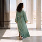 Back view of a woman wearing a floor-length sage green kaftan in a sunlit courtyard setting.