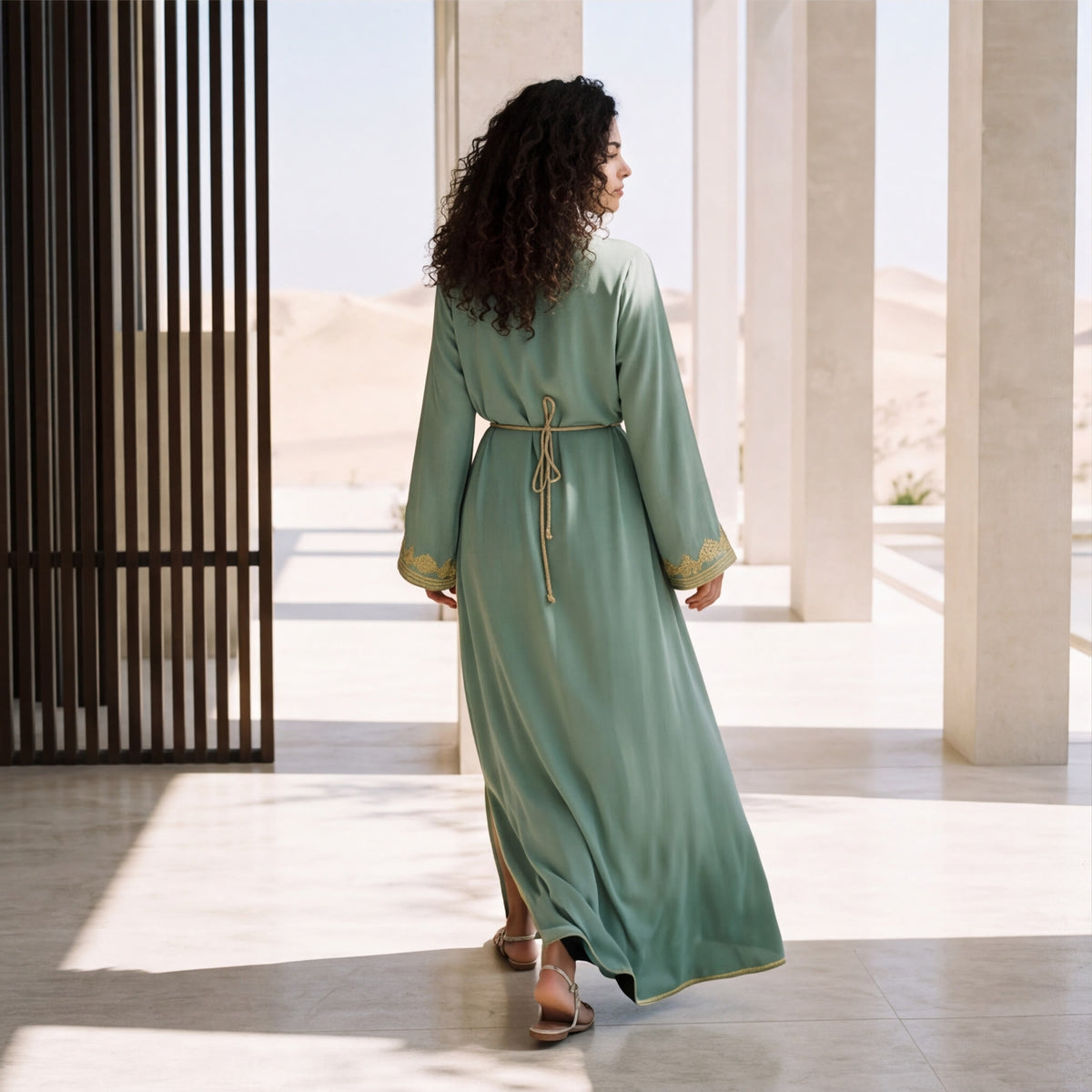 Back view of a woman wearing a floor-length sage green kaftan in a sunlit courtyard setting.